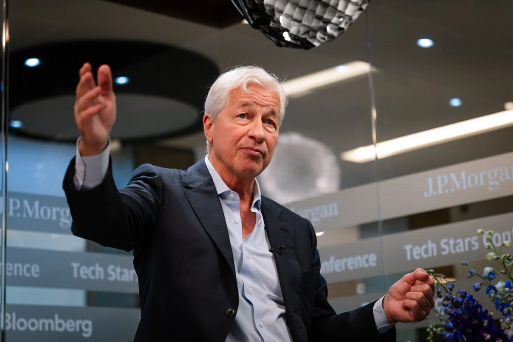 This image is intended to illustrate leadership, banking, and financial industry insights. It shows a senior business executive speaking at a professional event, with J.P. Morgan branding visible in the background. The image can be used for articles about banking, finance, business leadership, investment, technology in finance, or Wall Street trends.