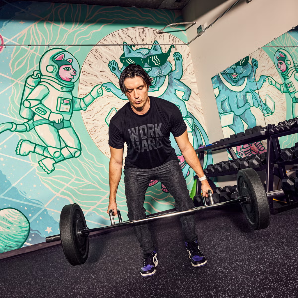 This image showcases strength training and fitness, highlighting a person performing a barbell exercise in a modern gym environment.