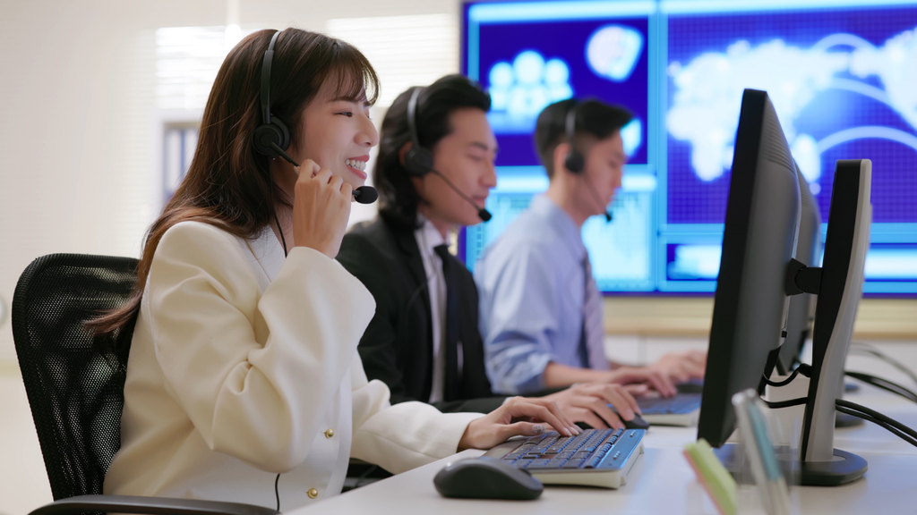 This image shows a professional customer support/call center team working at computers while wearing headsets. It represents customer service, technical support, call center operations, communication, and remote assistance in a modern workplace.