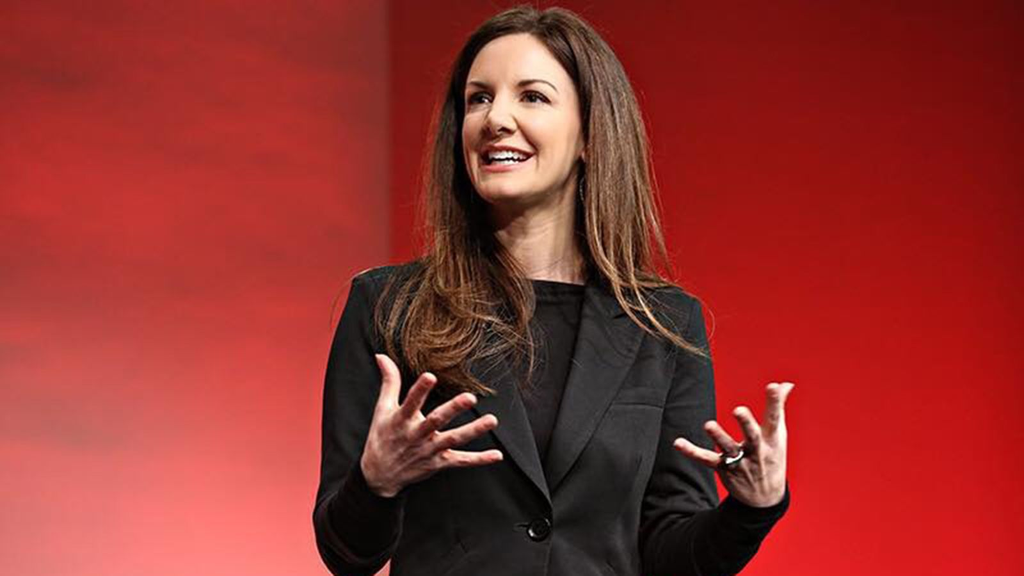 The image depicts a woman delivering a presentation or speech at a professional event, conference, or public speaking engagement.